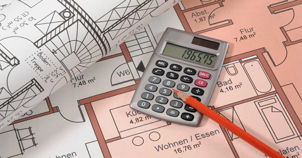 Auf dem Grundrissplan einer Immobilie liegen ein weiterer zusammengerollter Grundrissplan, ein Taschenrechner und ein Stift | Immobilienfinanzierung